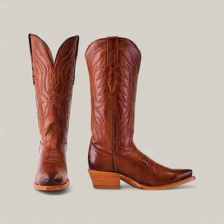 The Miranda Clayton Cogañac Leather Sole boots, with a mid shaft and snip toe, are made from premium brown leather. They showcase decorative stitching and a pointed toe design. One boot stands upright while the other is angled, highlighting the stacked heel and intricate details against a plain backdrop.