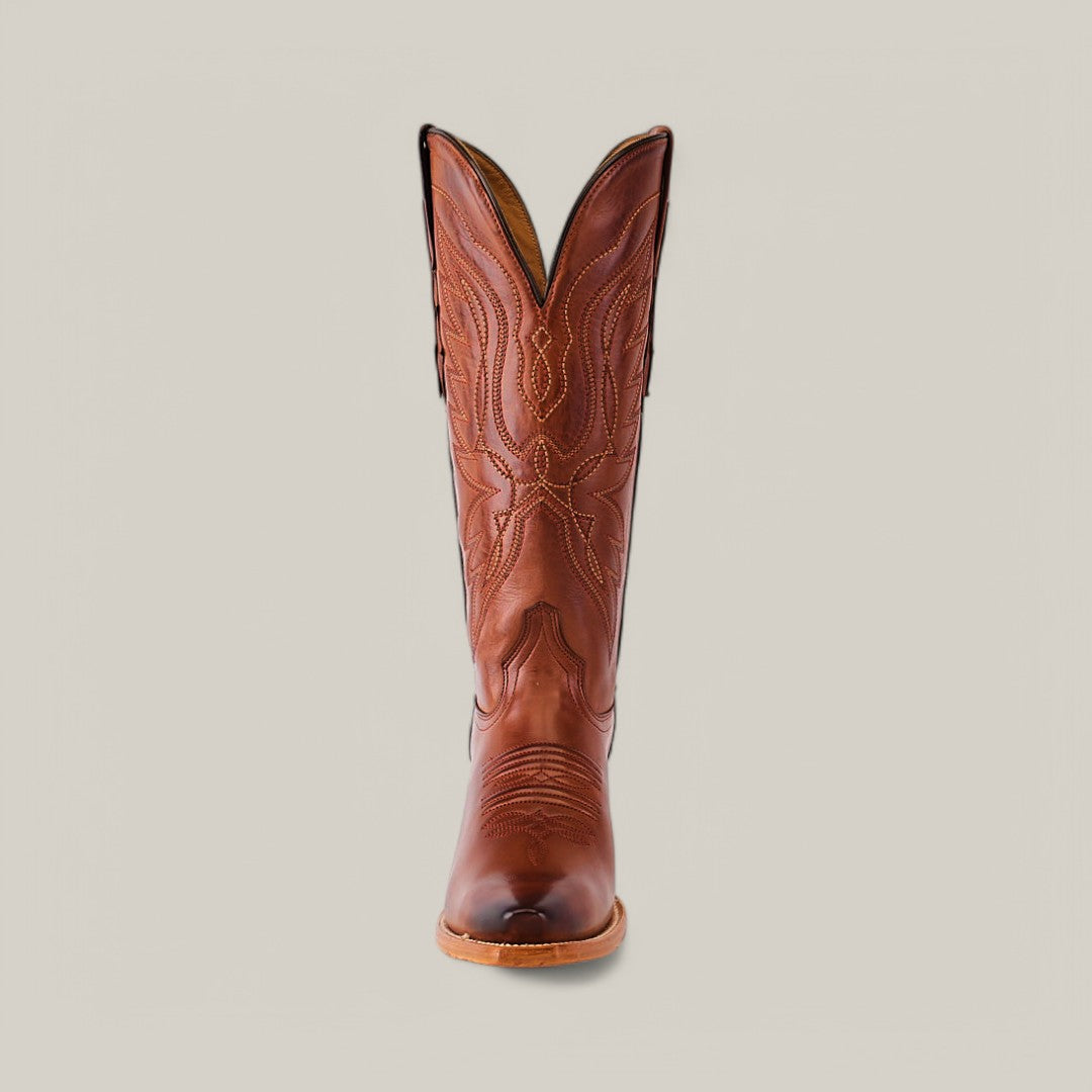 The Miranda Clayton Cogañac Leather Sole boot features a snip toe, premium brown leather with intricate stitching, and a high curved top. It stands upright against a plain light background, showcasing its decorative patterns.