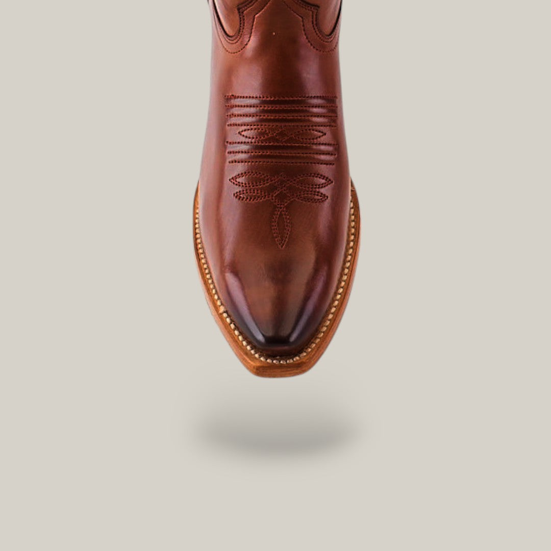 The Miranda Clayton Cogañac cowboy boot features a premium leather construction with intricate stitching on a plain background. It boasts a snip toe design and decorative edging, all enhanced by its durable leather sole.