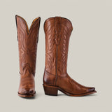 A pair of Miranda Clayton Brown Leather Sole cowboy boots with intricate stitching is displayed. One boot stands upright, while the other tilts forward, showcasing its snip toe and stacked heel against a plain backdrop.