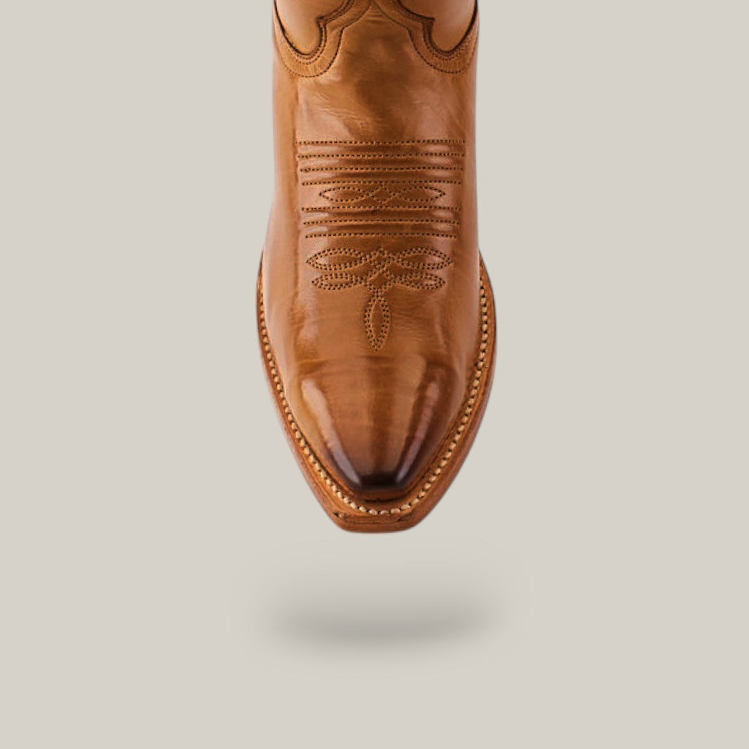 A single Miranda Clayton boot, featuring intricate stitching on the snip toe, is captured from above. The brown leather with a mid shaft design and gold leather sole stands elegantly against a plain light background.