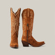 A pair of Kellie Suede Caramel Leather Sole cowboy boots, tall shaft with snip toe design, features detailed white stitching and side zippers. One boot stands upright while the other shows off the slanted heel against a neutral gray background.