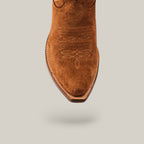 A close-up of the Kellie Suede Caramel Leather Sole boot highlights its snip toe design and intricate stitching. The tall-shaft cowboy boot is showcased against a simple beige background.