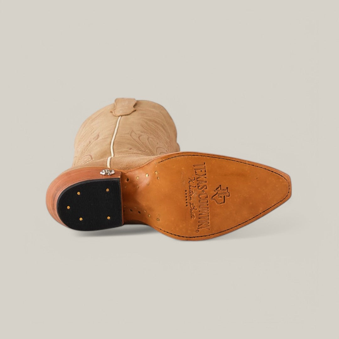 A Kellie Suede Fawn lies on its side against a plain background, showcasing its premium leather sole with the Texas Cowboy inscription and logo. The boot features a snip toe design and ornate stitching.