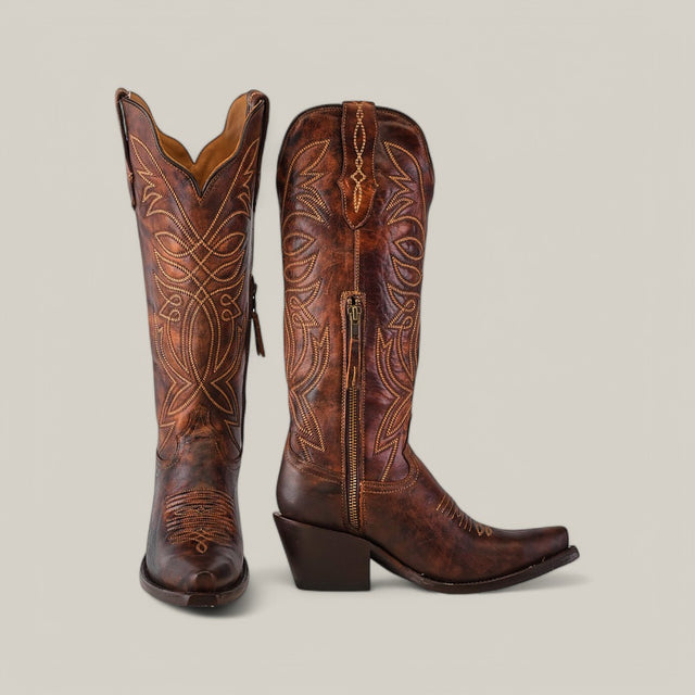 The Kellie Rustic Brown Leather Sole boots have a tall shaft and snip toe design, featuring intricate golden stitching and decorative side patterns. The left boot stands upright while the right is angled to showcase these stunning details.