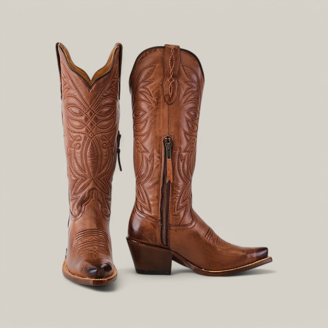 The Kellie Clayton Brown Leather Sole boots exude Western elegance with ornate stitching. One boot stands upright while the other leans slightly, highlighting their snip toes and stacked heels. A side zipper is visible on one boot against a light gray background.