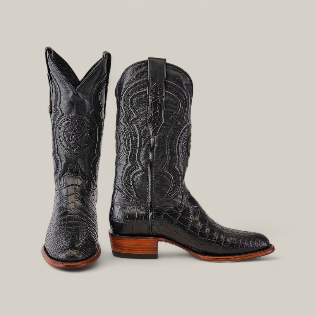 The product is the Exotic American Alligator Belly - Black - Roper Toe boot, featuring elegant black cowboy boots with intricate embroidery and a crocodile skin pattern. One boot stands upright, while the other is angled to showcase the wooden heel and detailed stitching typical of classic roper toe boots.