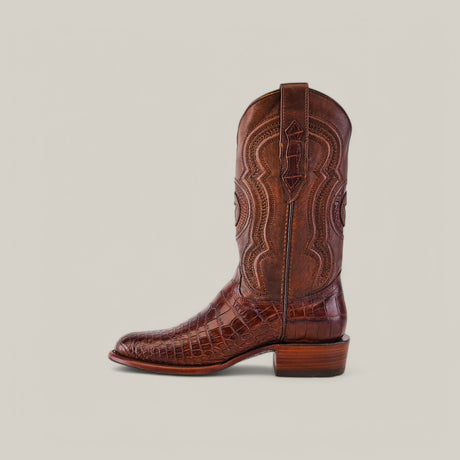 The Exotic American Alligator Belly cowboy boot in brown features a roper toe design with intricate stitching and a textured crocodile skin appearance on the toe and vamp. This boot offers exotic leather elements, a stacked heel, and convenient pull straps against a plain light beige background.