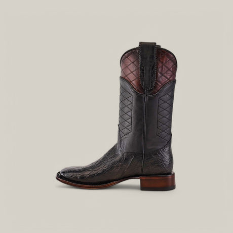 The Exotic American Alligator boot in dark gray boasts exceptional craftsmanship with a square toe and quilted stitching on the shaft, complemented by a brown heel and upper trim. Its set against a plain light gray background.