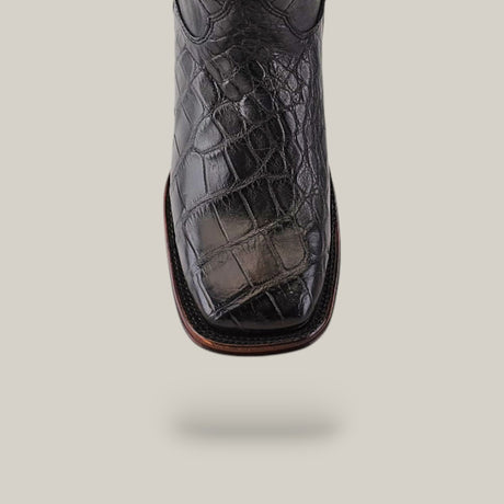 A close-up of an Exotic American Alligator boot with a square toe in dark gray against a light gray background. The surface reflects light, showcasing exceptional craftsmanship and highlighting its texture.