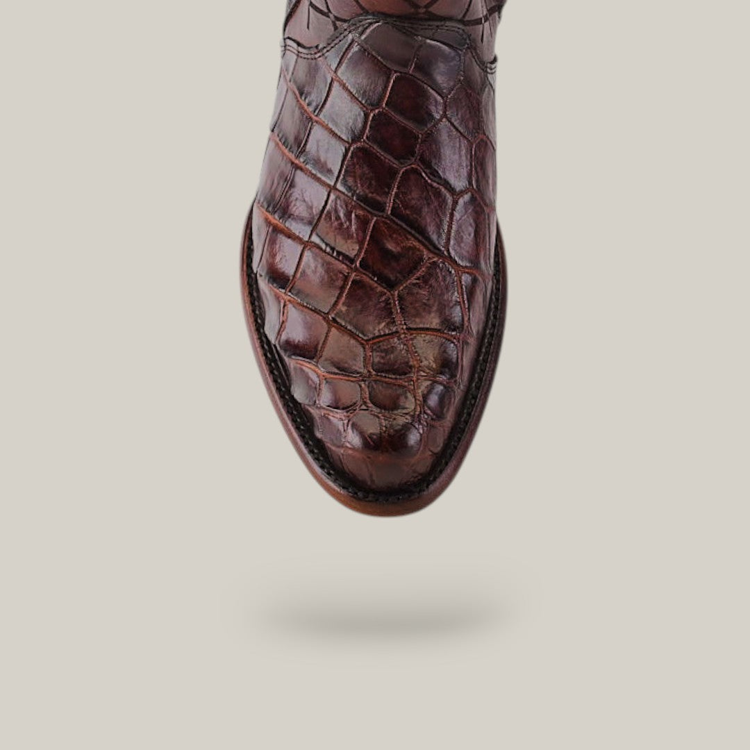 Close-up of an Exotic American Alligator boot in Europe Brown with a round toe, highlighting the glossy, textured leather. This handcrafted boot stands out against a light background, showcasing its luxurious material and intricate stitching.