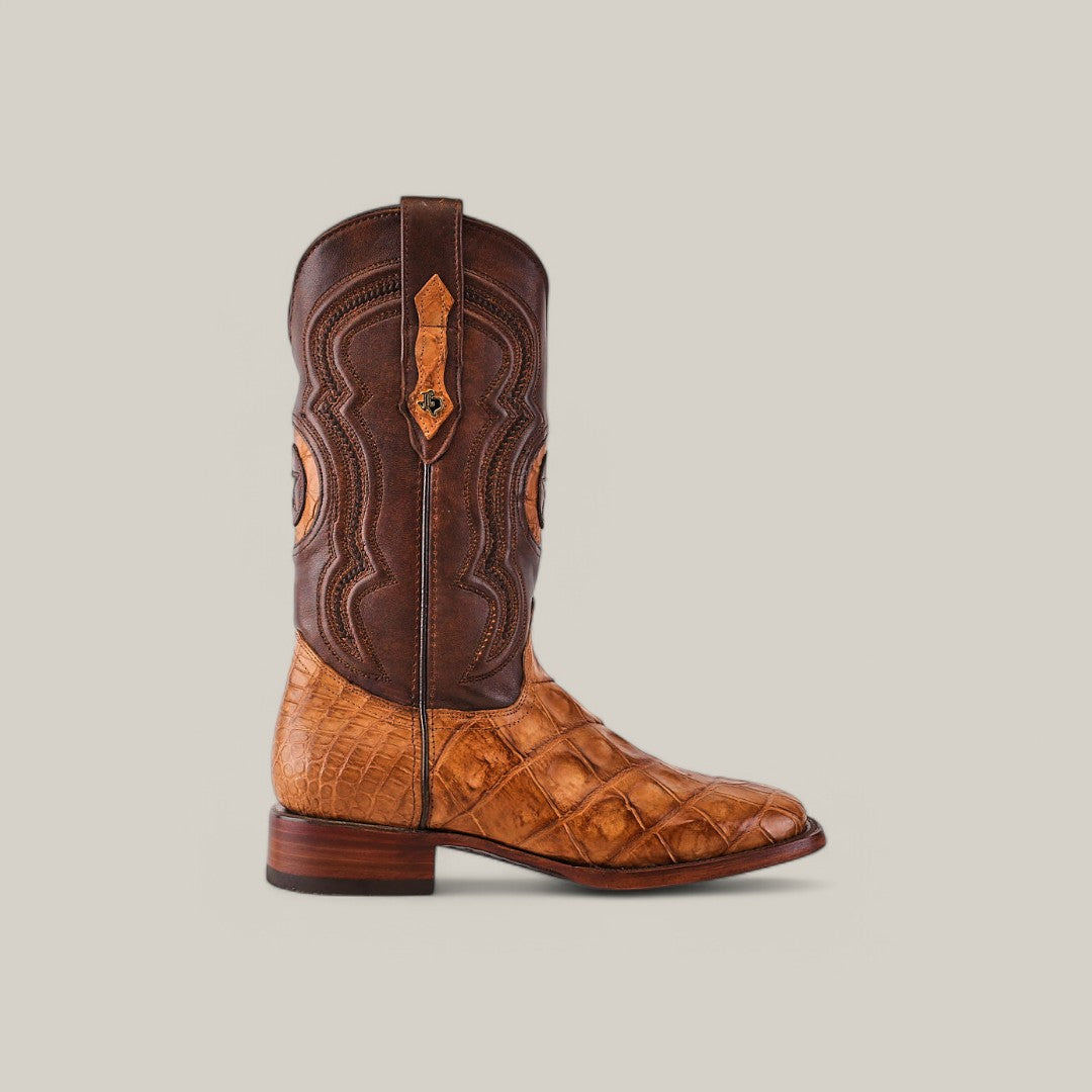 The Exotic American Alligator Hornback - Fawn - Square Toe cowboy boot features sophisticated craftsmanship with a textured tan leather lower, smooth brown upper, detailed stitching, side pull strap, and a low wooden heel. Its charm is enhanced by the square toe design against a light gray background.