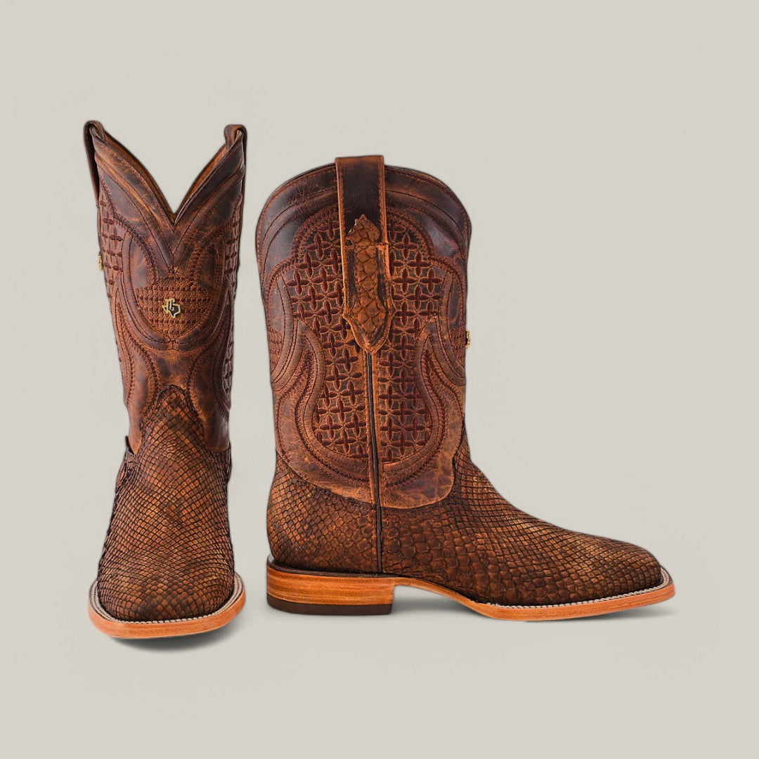 The Exotic Python - Tamarindo cowboy boots feature intricately designed textured python leather with detailed stitching. One boot is upright with a square toe, while the other is flat, showcasing its craftsmanship against a light grey background.