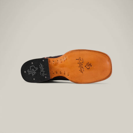 The image displays the bottom view of a handcrafted mens shoe, featuring an exotic leather sole with decorative stitching. The sole has branding and logo engravings in black and brown. A plain light background highlights the details of these Exotic Caiman Belly - Black Cherry - Square Toe boots.