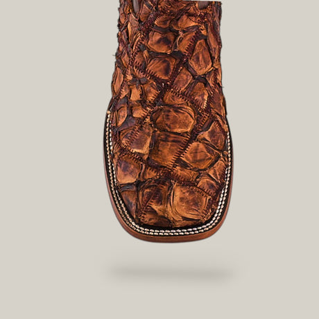 Close-up of the Exotic Patchwork Pirarucu Fish - Matte Brown - Square Toe boot, showcasing its unique textured pattern and detailed stitching, set against a plain light beige background.