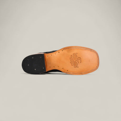 A close-up of the Exotic Patchwork Python - Black - Square Toe shows a light brown leather sole with fine stitching, the brand logo near the arch, and a black heel accented by small metal studs.