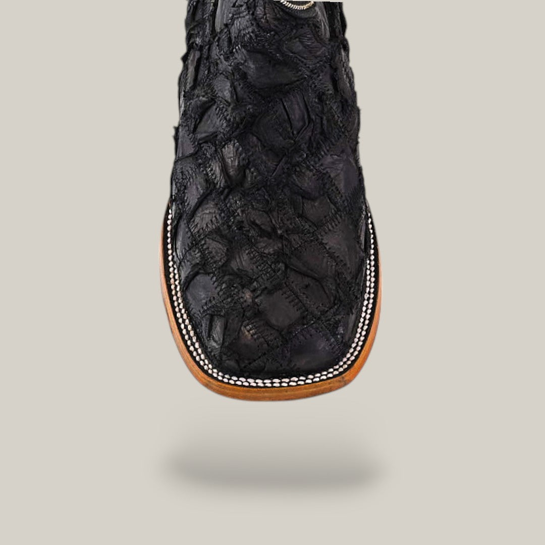 A close-up of the Exotic Patchwork Pirarucu Fish boot in matte black, featuring a square toe, eco-friendly textured fish leather, detailed stitching, and light brown and white trim, set against a plain light background.