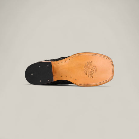 A close-up of the Exotic Patchwork Pirarucu Fish - Matte Black - Square Toe sole shows a tan eco-friendly leather section with branding and a black textured heel, set against a plain light gray background.