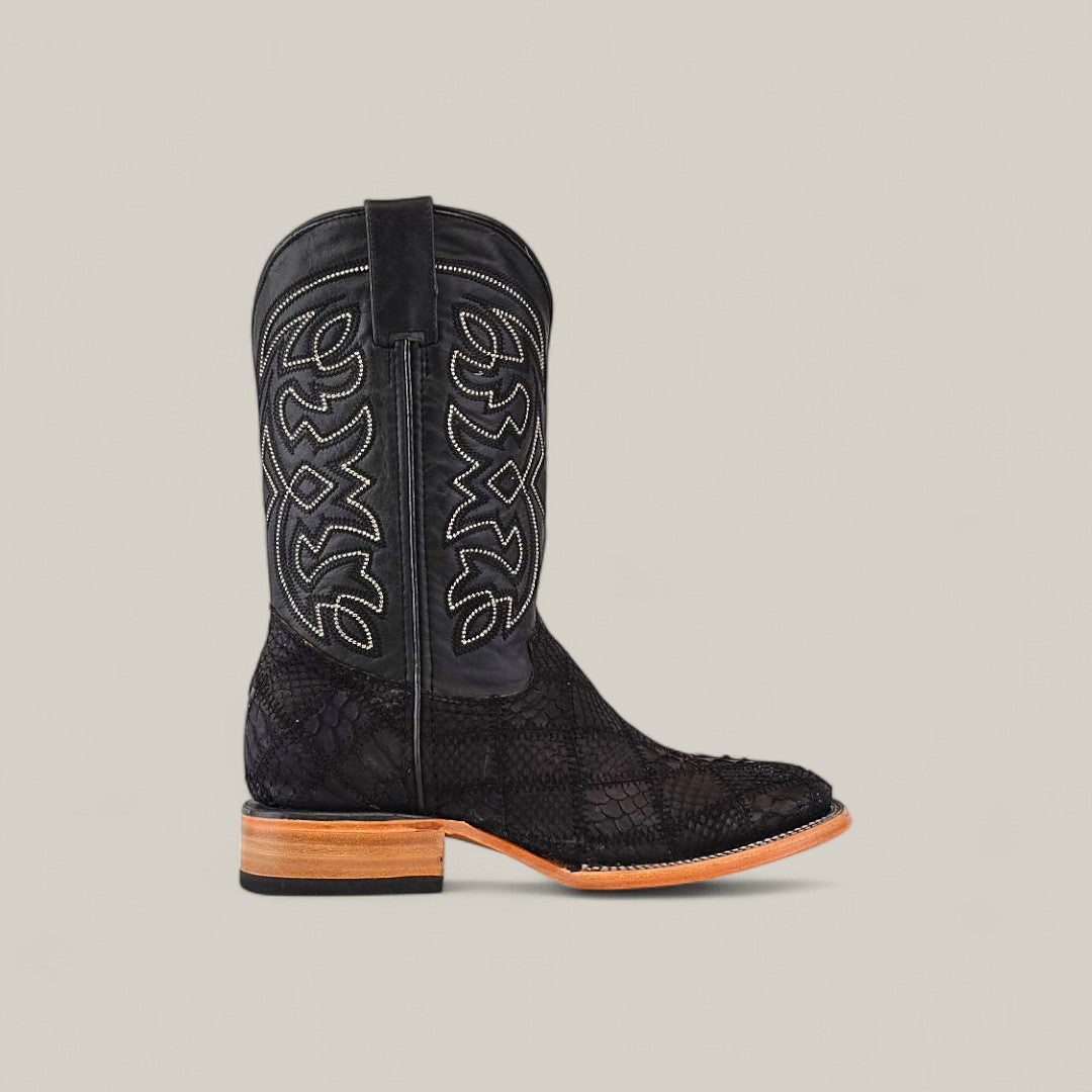 The Exotic Patchwork Python - Matte Black - Square Toe is a single cowboy boot with light stitching on the shaft, a textured python pattern below, and a light brown wooden heel. Displayed on a plain light beige background.