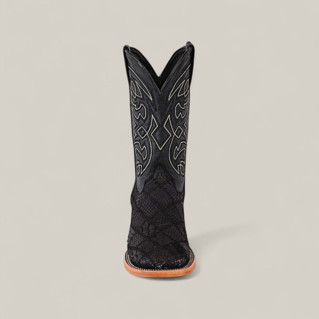 The Exotic Patchwork Python - Matte Black - Square Toe boot, featuring decorative stitching, textured patterns, and a light brown sole, stands upright against a plain light gray background.