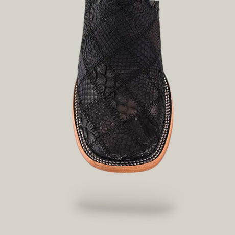 Close-up of the square toe design on the Exotic Patchwork Python - Matte Black boot, featuring a snakeskin pattern, white stitching, and a light brown sole against a plain light background.
