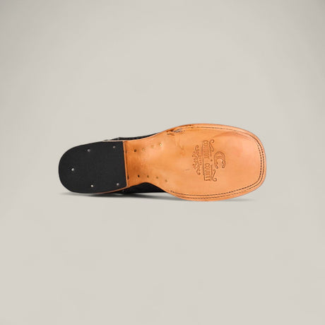 The image shows the bottom view of the Exotic Patchwork Python - Matte Black - Square Toe dress shoe, featuring a tan leather sole with visible stitching, small metal tacks, and the brand name and logo stamped near the arch.