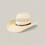 The 50x Brazil Straw Hat features a light beige color, wide brim for sun protection, decorative crown cutouts, and a black hatband with silver accents—ideal for effortless summer style against a plain background.