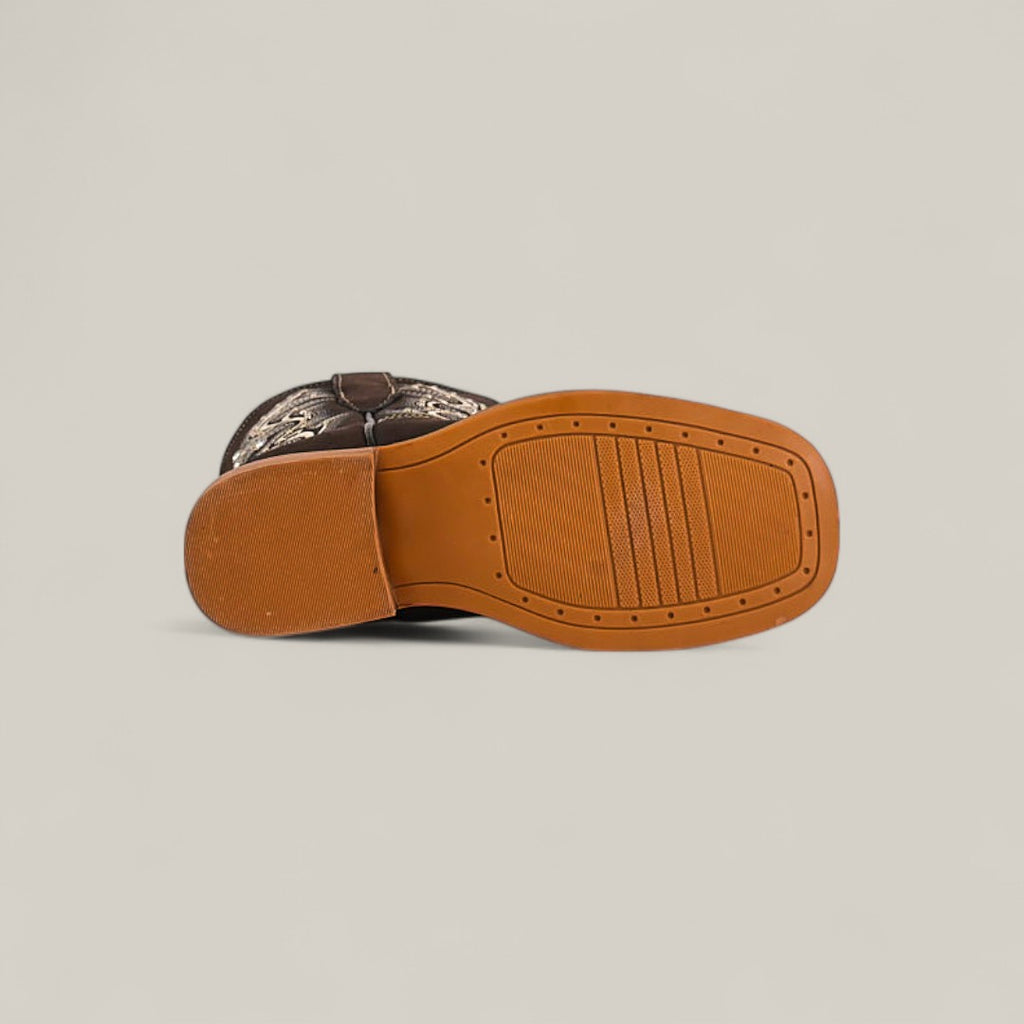 The Amara Suede Oxford - Square Toe Kids Boot is shown on its side, highlighting a tan rubber tread sole and a brown and beige stitched design on the upper, showcasing stylish craftsmanship.