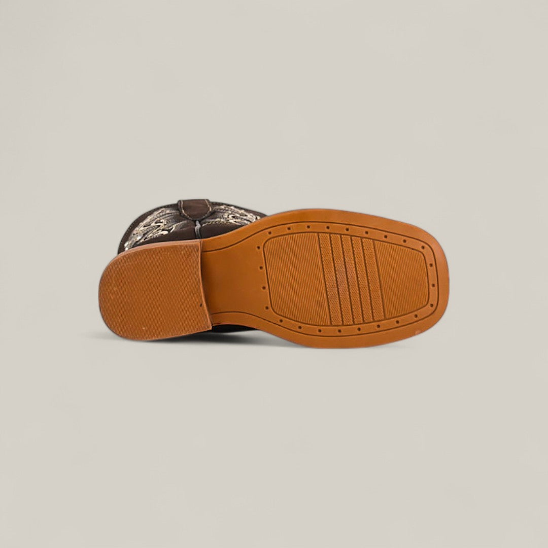 The Amara Suede Oxford - Square Toe Kids Boot is shown on its side, highlighting a tan rubber tread sole and a brown and beige stitched design on the upper, showcasing stylish craftsmanship.
