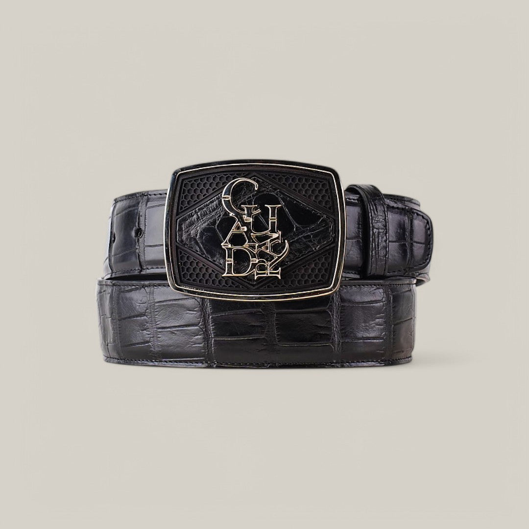 The Alligator Belly Black - Narrow Square Toe - IMPERIO is a black leather belt with a crocodile pattern and an abstract-embossed metallic square buckle, neatly coiled on a light gray background.