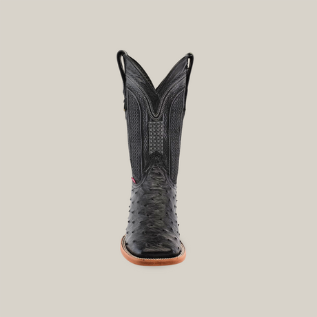 The Exotic Full Quilt Ostrich - Black - Square Toe boot, crafted from exotic ostrich leather, showcases detailed stitching and a textured pattern on the toe and shaft. It has side pull tabs, a tan sole, and is set against a beige background.