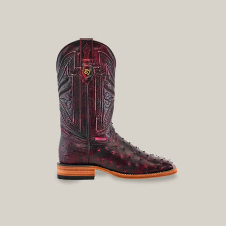 The Exotic Full Quilt Ostrich - Black Cherry - Square Toe boot features genuine ostrich leather with a textured burgundy upper, ornate stitching, and brass embellishments. Its light brown sole and small heel add allure, all set against a plain off-white background.