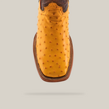 A close-up of the Exotic Full Quilt Ostrich boot in buttercup showcases its square toe and textured pattern with a brown stitched border, set against a plain light gray background.