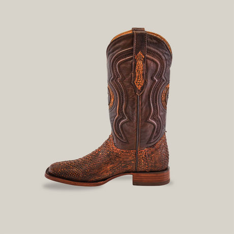 The Exotic Python - Rustic Cogñac boot showcases intricate stitching and textured leather in profile view. Predominantly cognac with orange accents, its detailed design and craftsmanship shine, while the square toe adds a modern touch against a plain, neutral background.