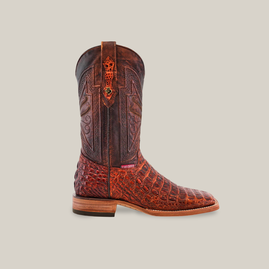 The Exotic Caiman Horn Back - Smoke Cogñac Square Toe boot features a handcrafted design with a brown top, textured red-brown Caiman leather lower section, intricate stitching on the shaft, and a small emblem. It has a light wood sole on a plain beige background.