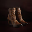 A pair of CUADRA Maple Embroidery & Crystals round-toe boots in brown leather with gold floral embroidery and bead detailing, featuring a side zipper and chunky heels, set against a dark background.