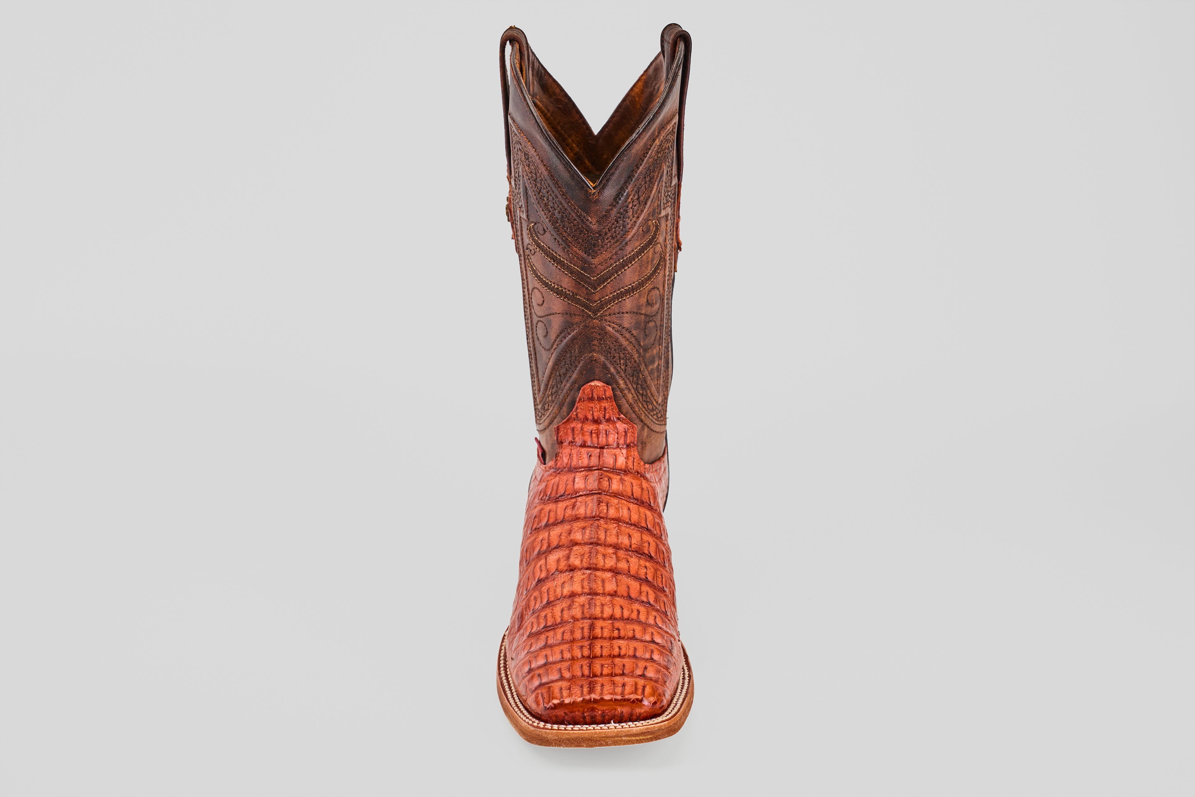 The Exotic Caiman Horn Back - Brandy - Square Toe boot, featuring a brown textured shaft and reddish patterned foot, is displayed facing forward on a plain light gray background.