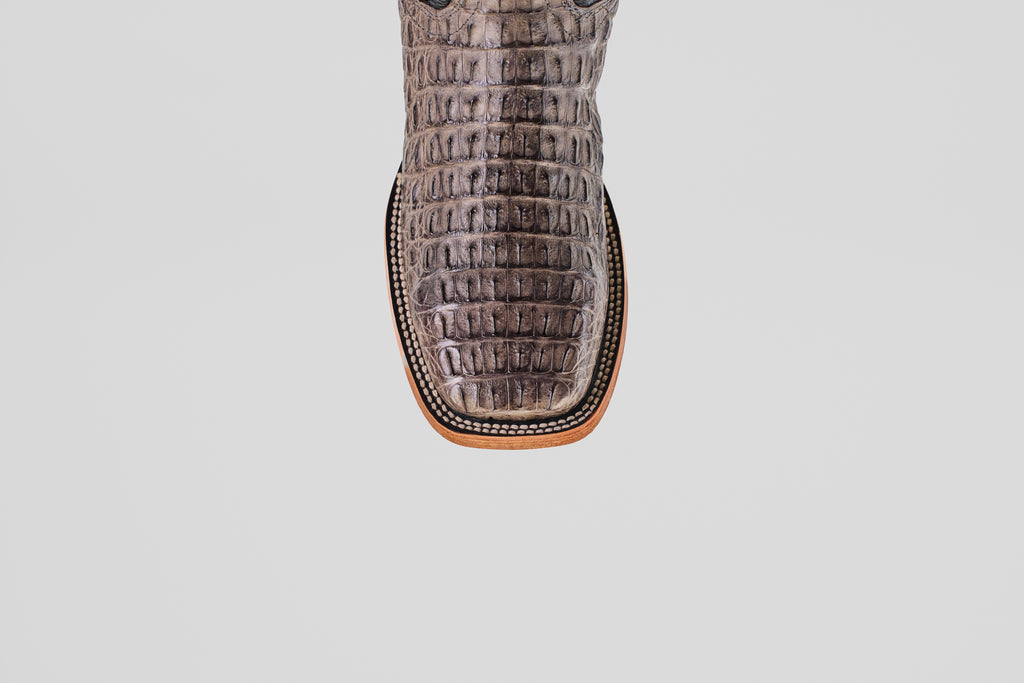 A close-up of the Exotic Caiman Horn Back - Serpentine - Square Toe boot’s brown, crocodile-embossed leather toe with detailed edge stitching, shown against a plain white background.
