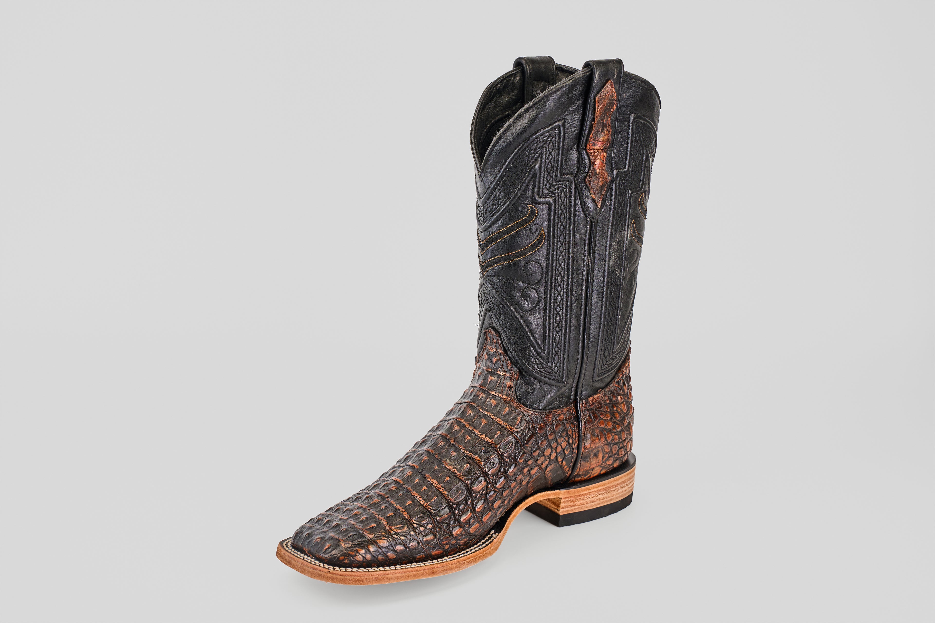 The Exotic Caiman Horn Back - Roma - Square Toe boot features a brown textured caiman leather foot and a tall black intricately stitched shaft, displayed against a plain light gray background.