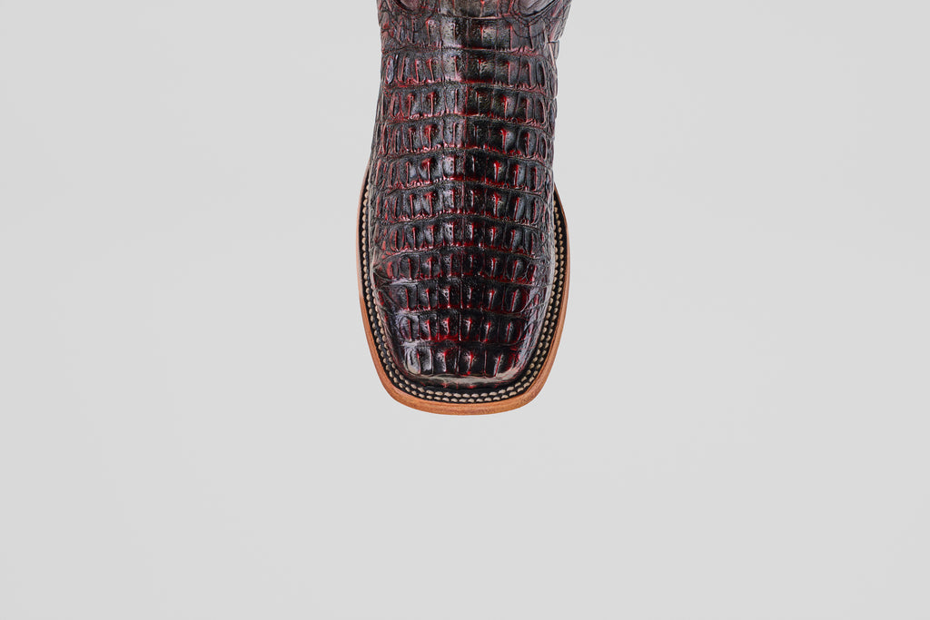 A close-up of the Exotic Caiman Horn Back - Black Cherry - Square Toe boot shows its dark crocodile pattern, square tip, and detailed stitching on the tan sole against a plain light background.
