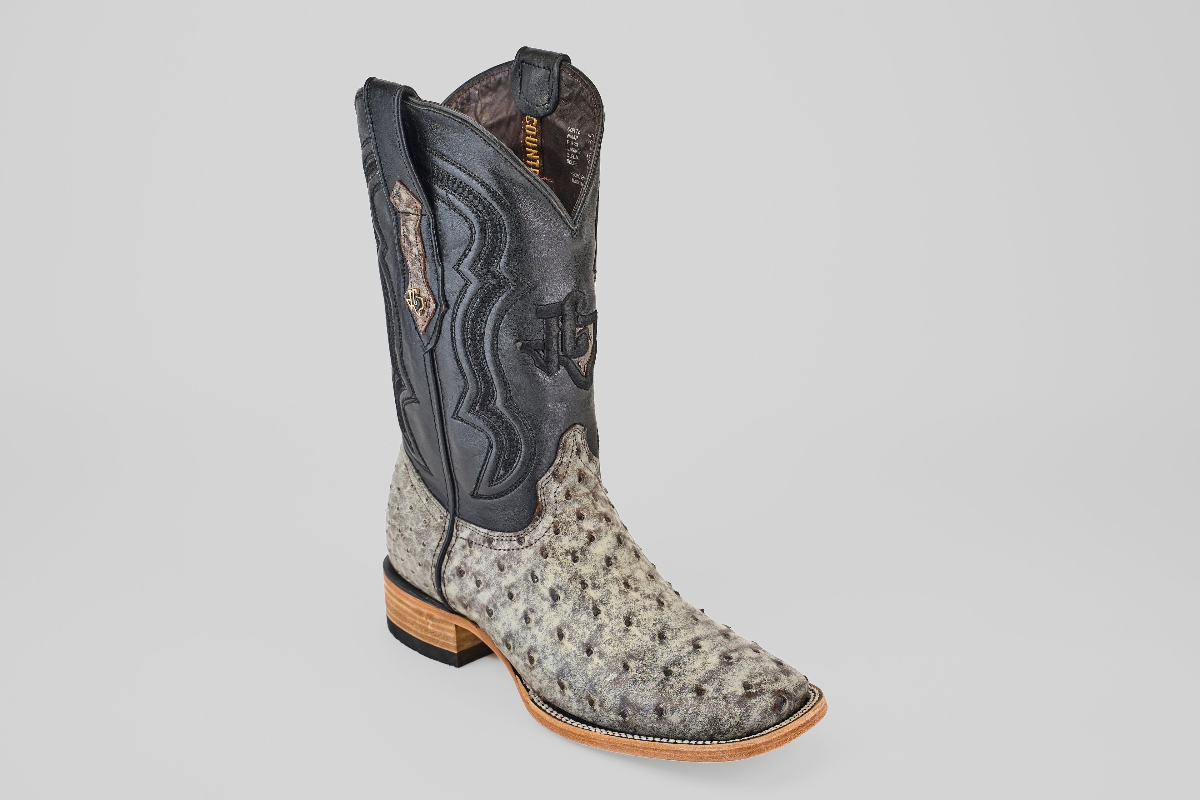 The Exotic Full Quill Ostrich - Nicotine - Square Toe men’s boot features a light gray ostrich lower, a black stitched upper shaft, and a wooden sole, showcased against a plain light background.
