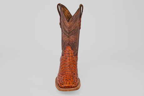The Exotic Caiman Head - Cogñac - Square Toe cowboy boot showcases brown caiman leather with intricate stitching and textured patterns, highlighted by a square toe, viewed from the front on a light gray background.