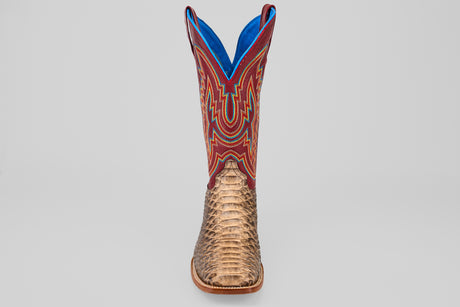 The Barlow - Taupe - Square Toe men’s statement boot features a textured taupe python leather lower, a vibrant red upper with blue and yellow stitching, and is displayed front-facing against a plain gray background.