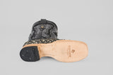 A close-up of the Exotic Pirarucu Fish - Newspaper - Square Toe boot showcases its black textured upper, light tan leather sole with embossed “TEXAS COUNTRY” branding, and a black logo heel cap on a gray background.