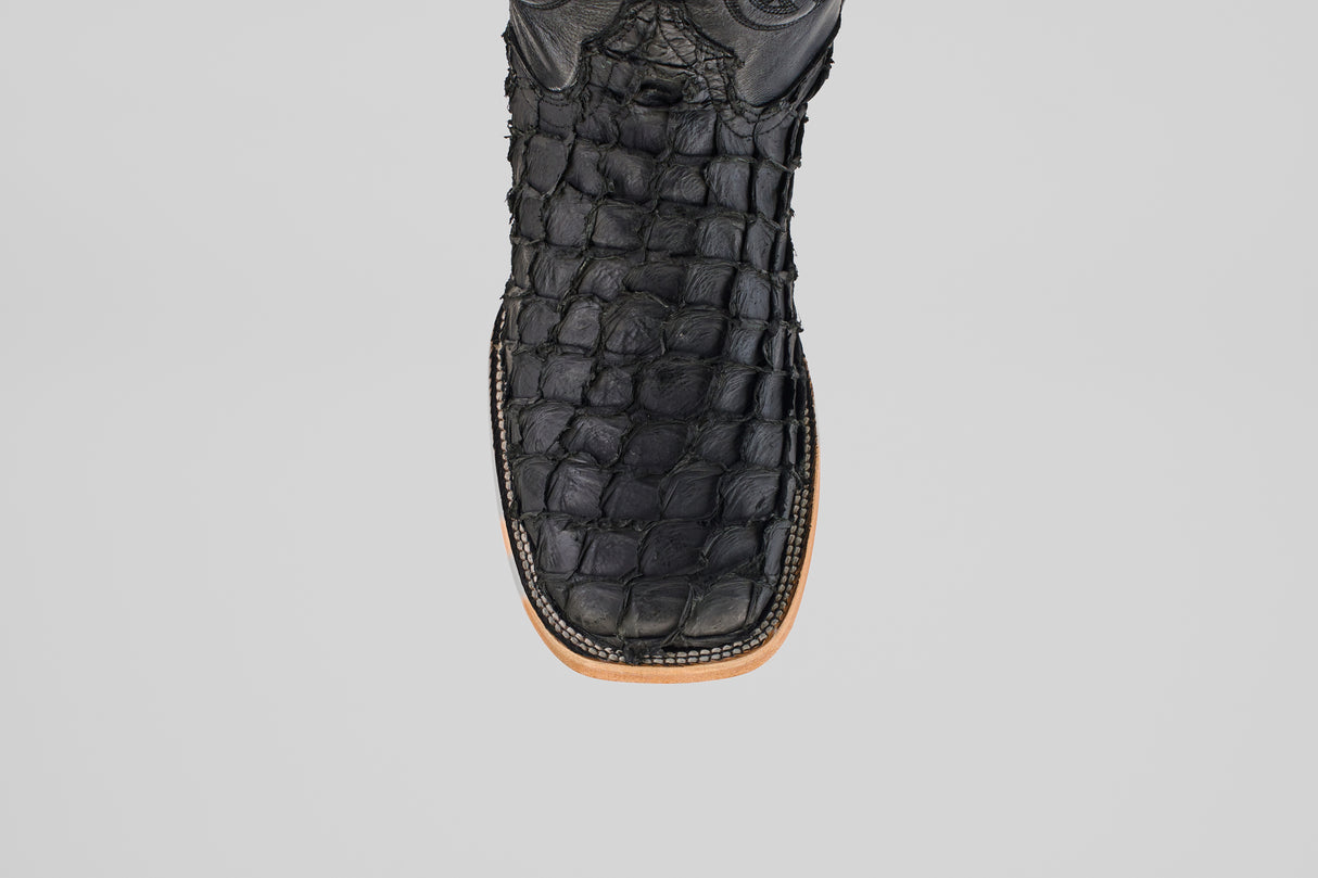 A close-up of the Exotic Pirarucu Fish boot in matte black, featuring a textured finish, square toe, and light brown sole, set against a plain light gray background.