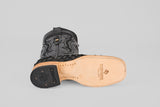 A black Exotic Pirarucu Fish boot with a square toe lies on its side, highlighting intricate stitching and the Texas Country logo on the sole—a striking mix of matte black textures and premium exotic leather.