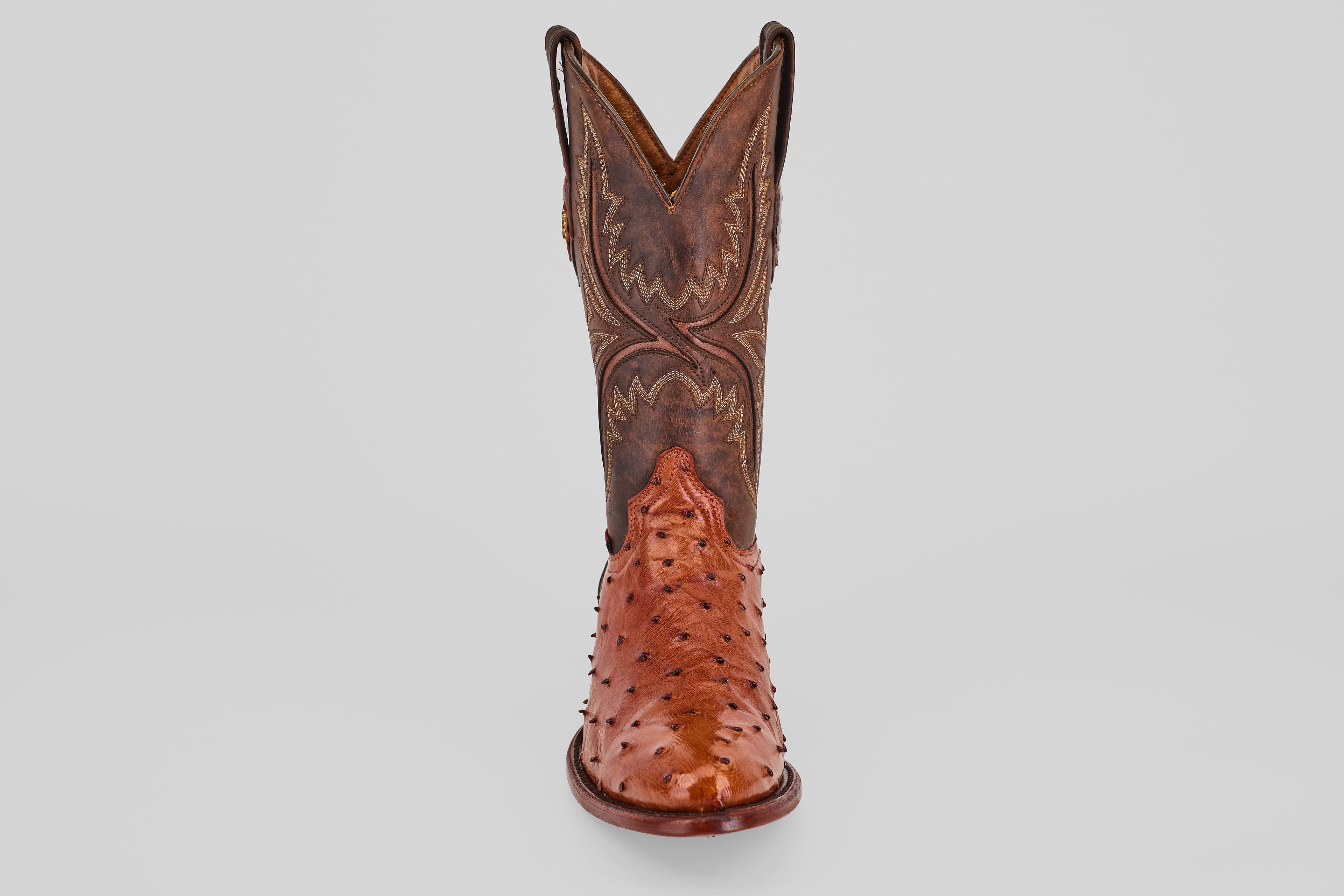 A single Exotic Full Quilt Ostrich - Brandy - Round Toe cowboy boot in brown, handcrafted with decorative stitching and a shiny quilted ostrich leather finish, shown from the front against a plain light background.