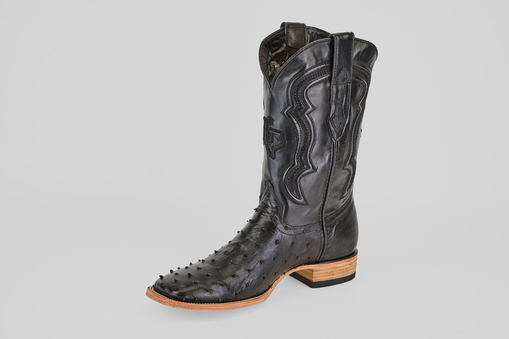 The Austin - Black - Square Toe cowboy boot features black Avestruz leather with decorative stitching, a textured finish, and a light brown wooden heel and sole, showcased against a plain light gray background.
