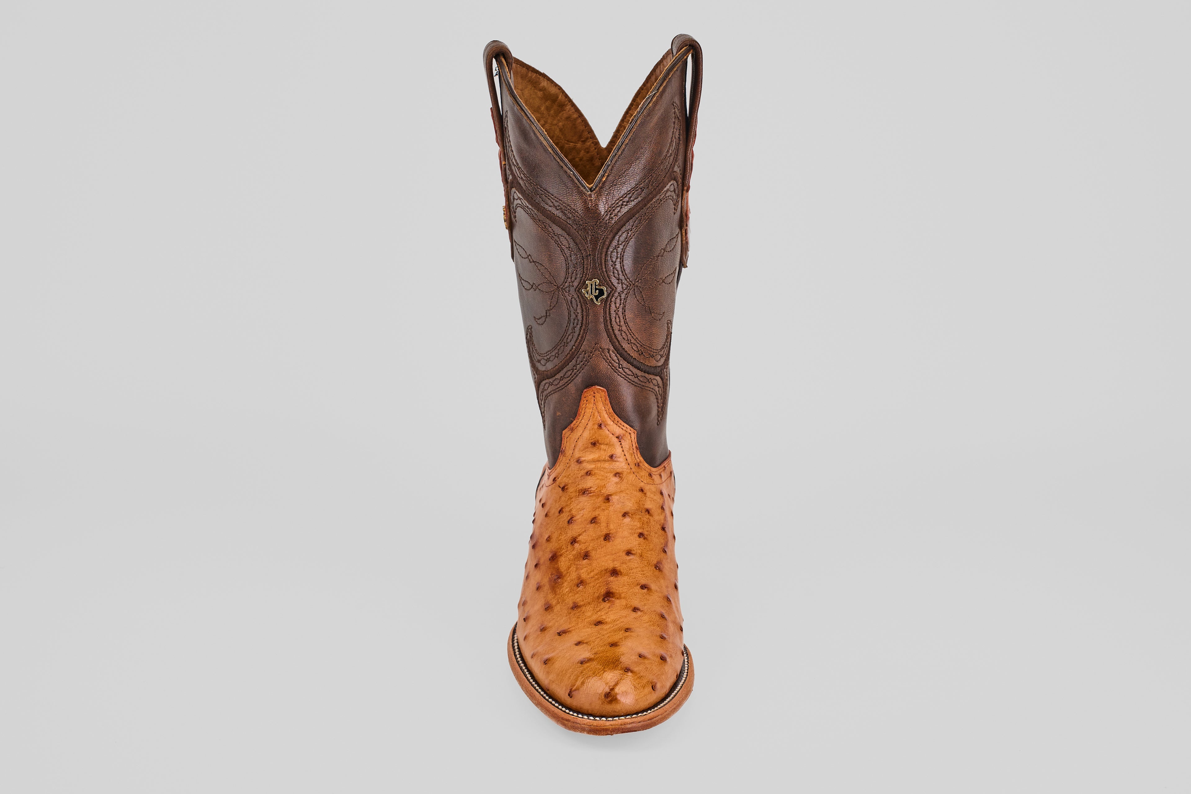 The Austin - Brandy - Roper Toe is a men's cowboy boot featuring a brown leather upper and light tan textured ostrich leather lower, shown upright on a plain white background. Ideal for fans of classic ostrich leather boots.