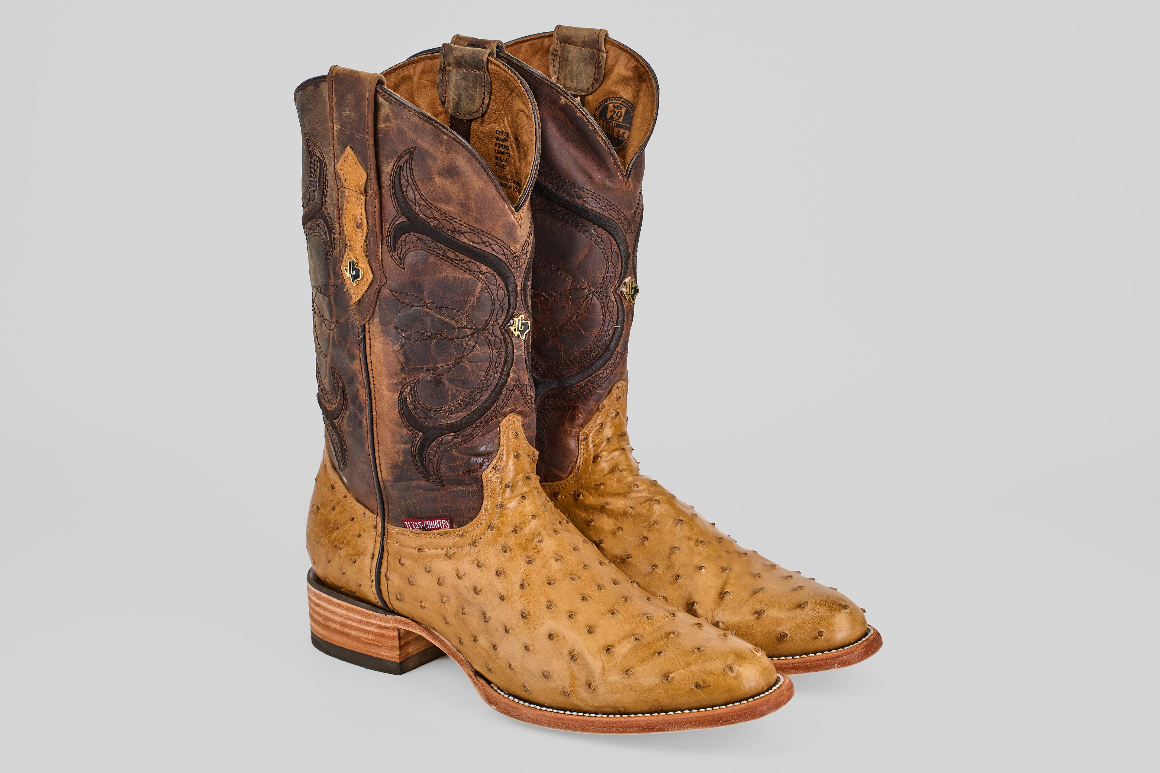 The Austin - Antique - Roper Toe boots feature tan ostrich leather on the foot and light brown, intricately stitched shafts, shown standing upright against a plain gray background.
